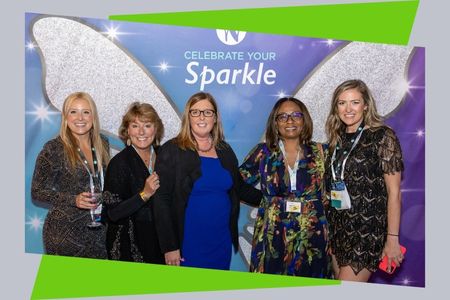 Five women standing and smiling in front of a backdrop that says "celebrate your sparkle"
