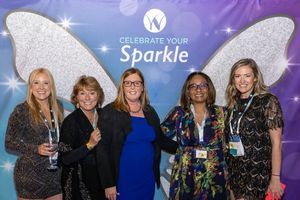 A photo of five women posing in front of a photo backdrop that says "Celebrate Your Sparkle"